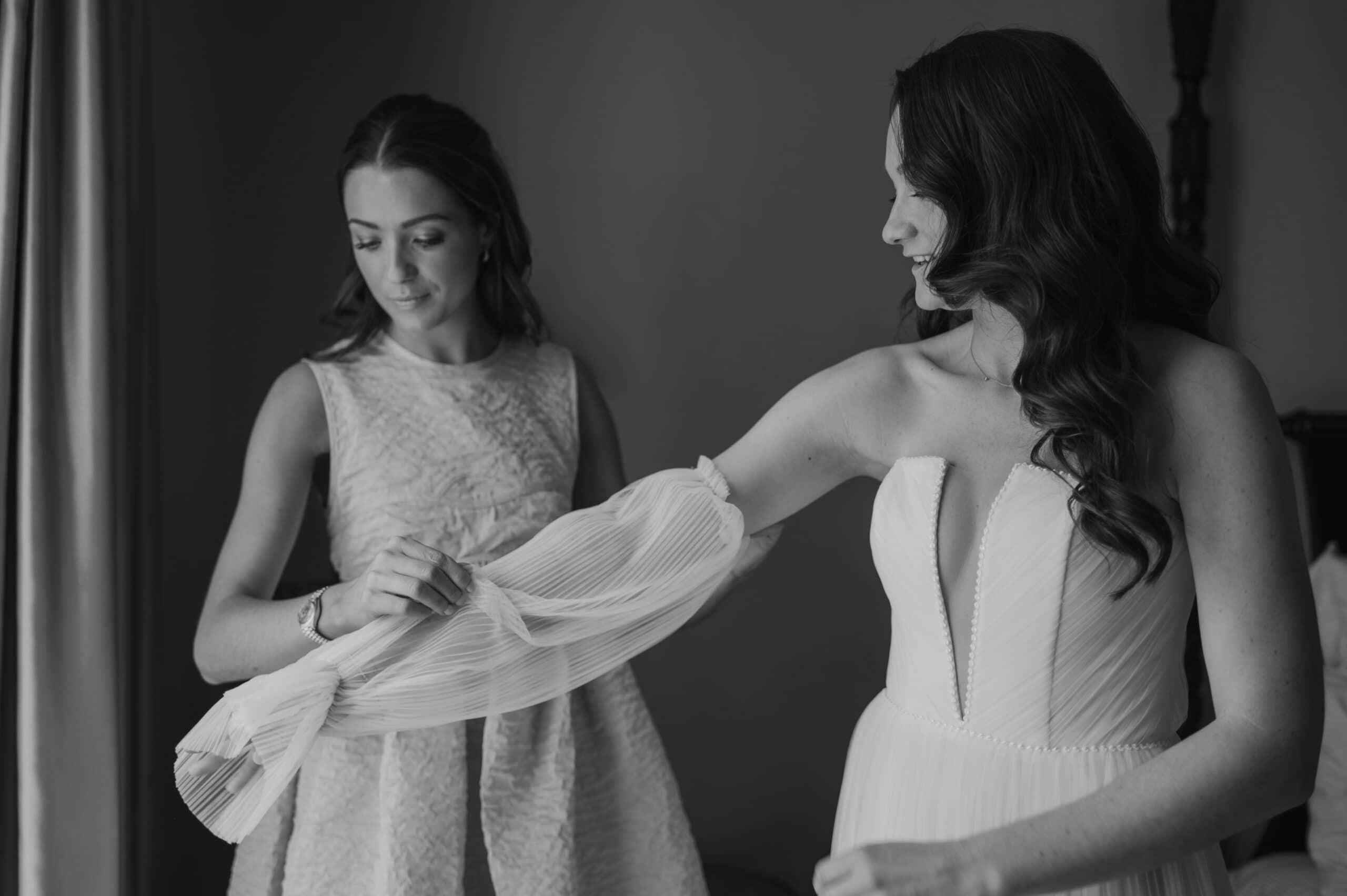 black and white image of bride being helped with her dress by bridesmaid