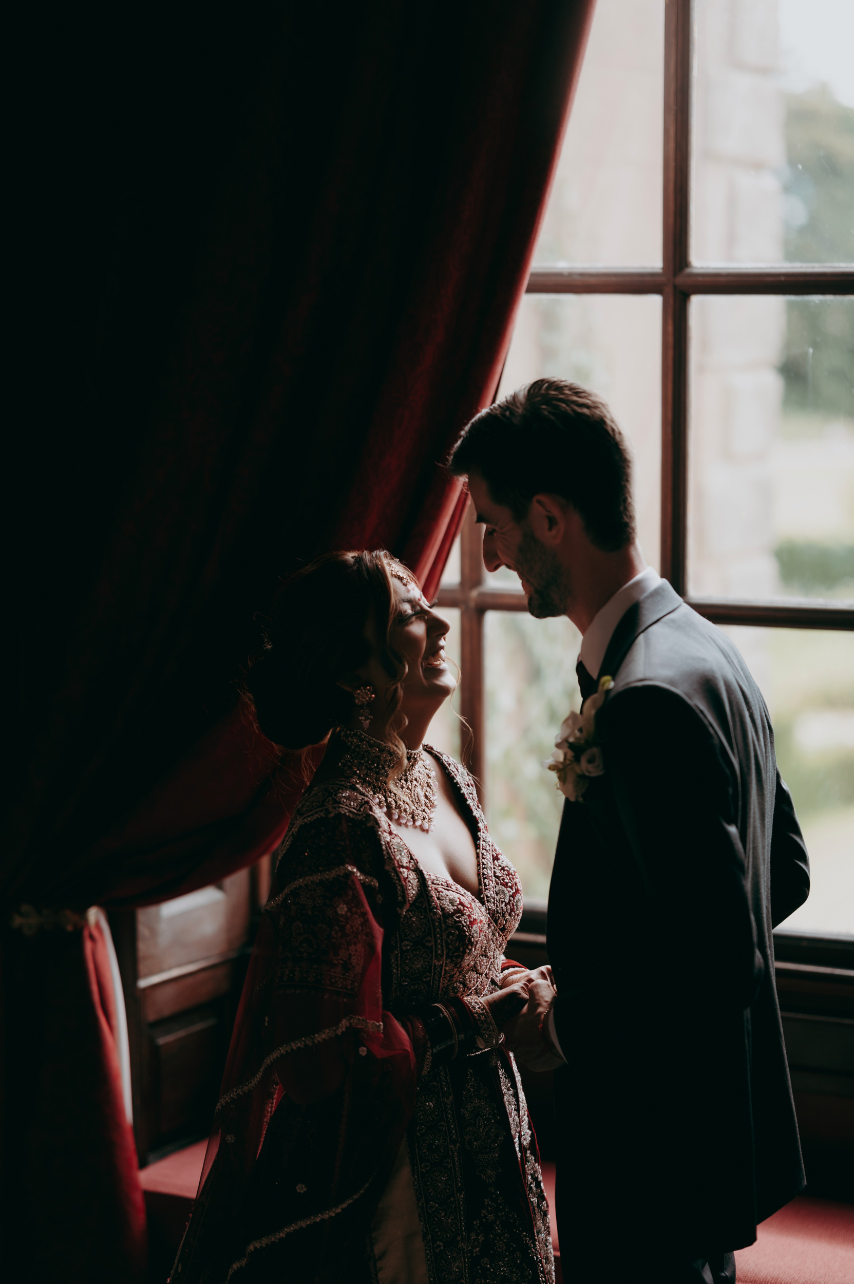 bride and groom laughing by window light during voews